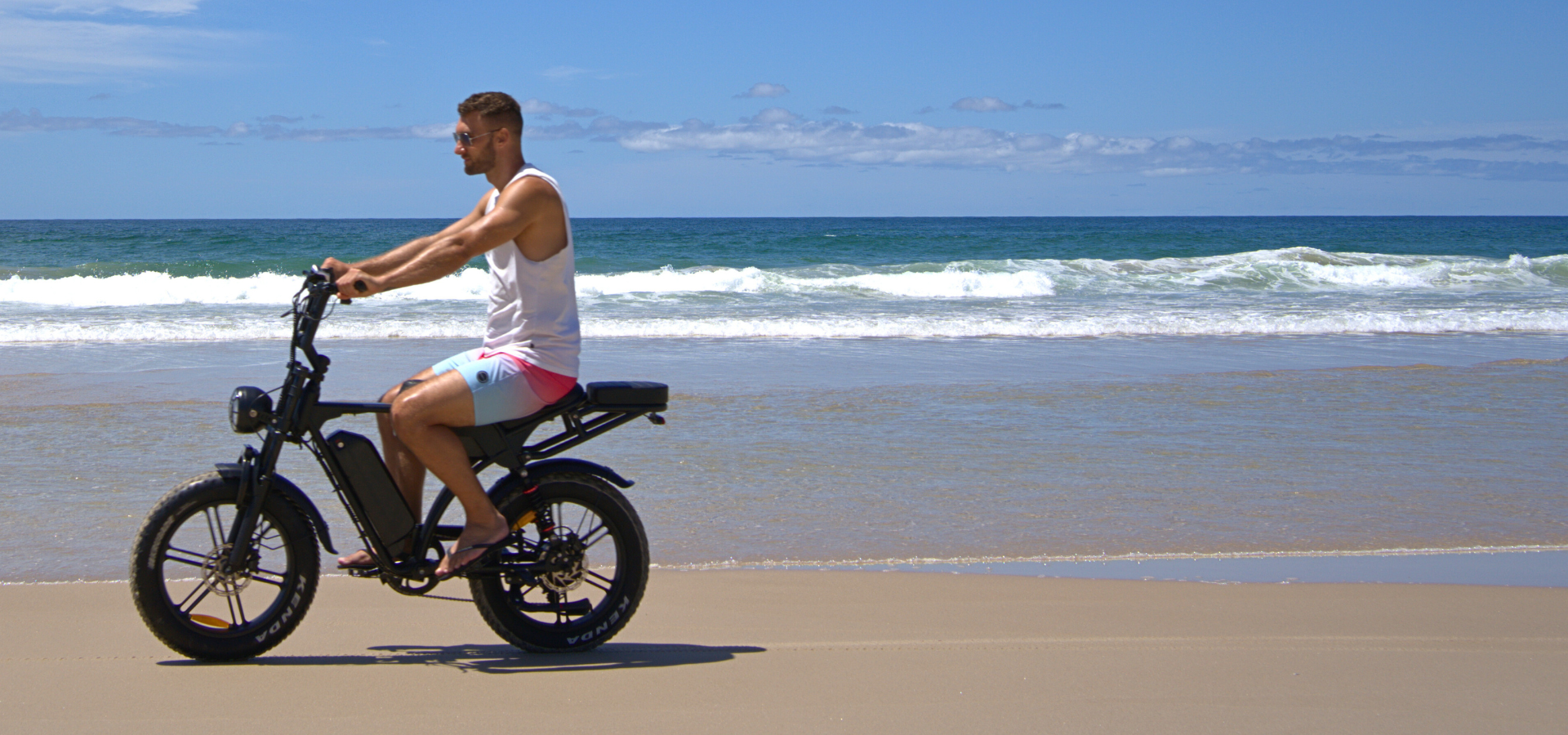 Man riding a dual battery fat tyre electric bike with NFC display lock along an Australian beach.