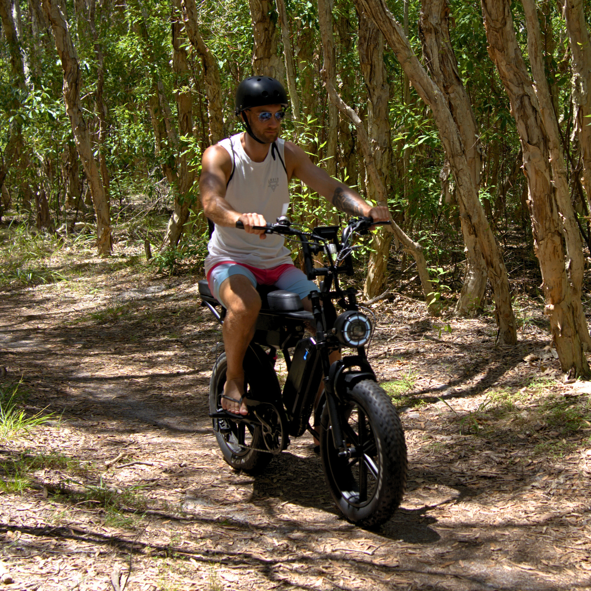 Fat tyre electric bike with dual battery system riding through a forest trail demonstrating off road performance.